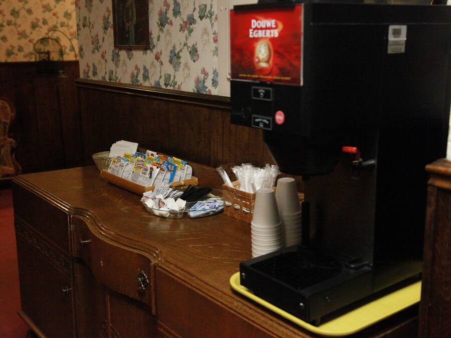 Una máquina de café con etiqueta Douwe Egberts, una cesta de aperitivos y vasos de papel apilados sobre una encimera de madera.