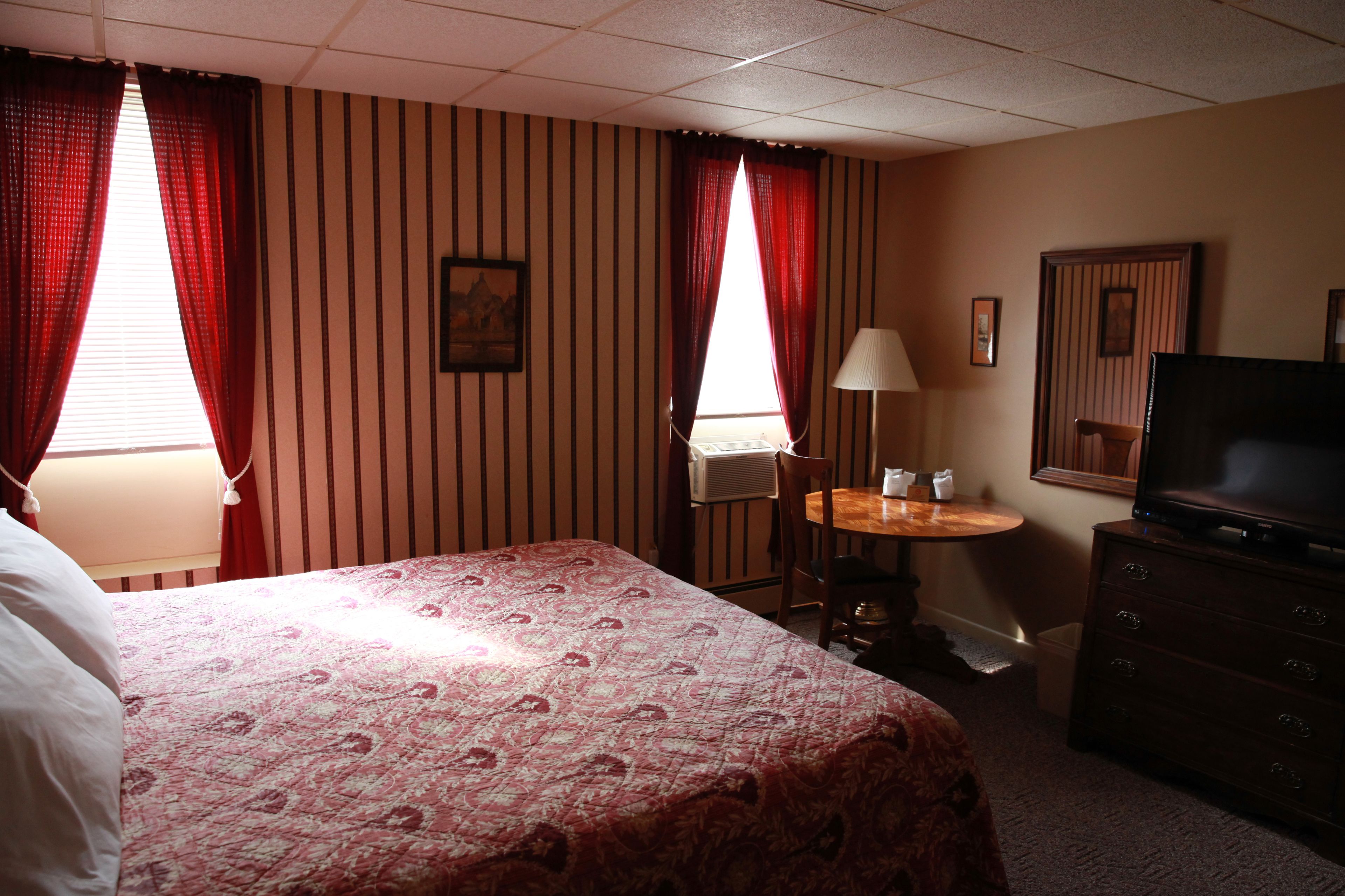 A hotel room with a bed, a desk with a chair, a TV, and a lamp.