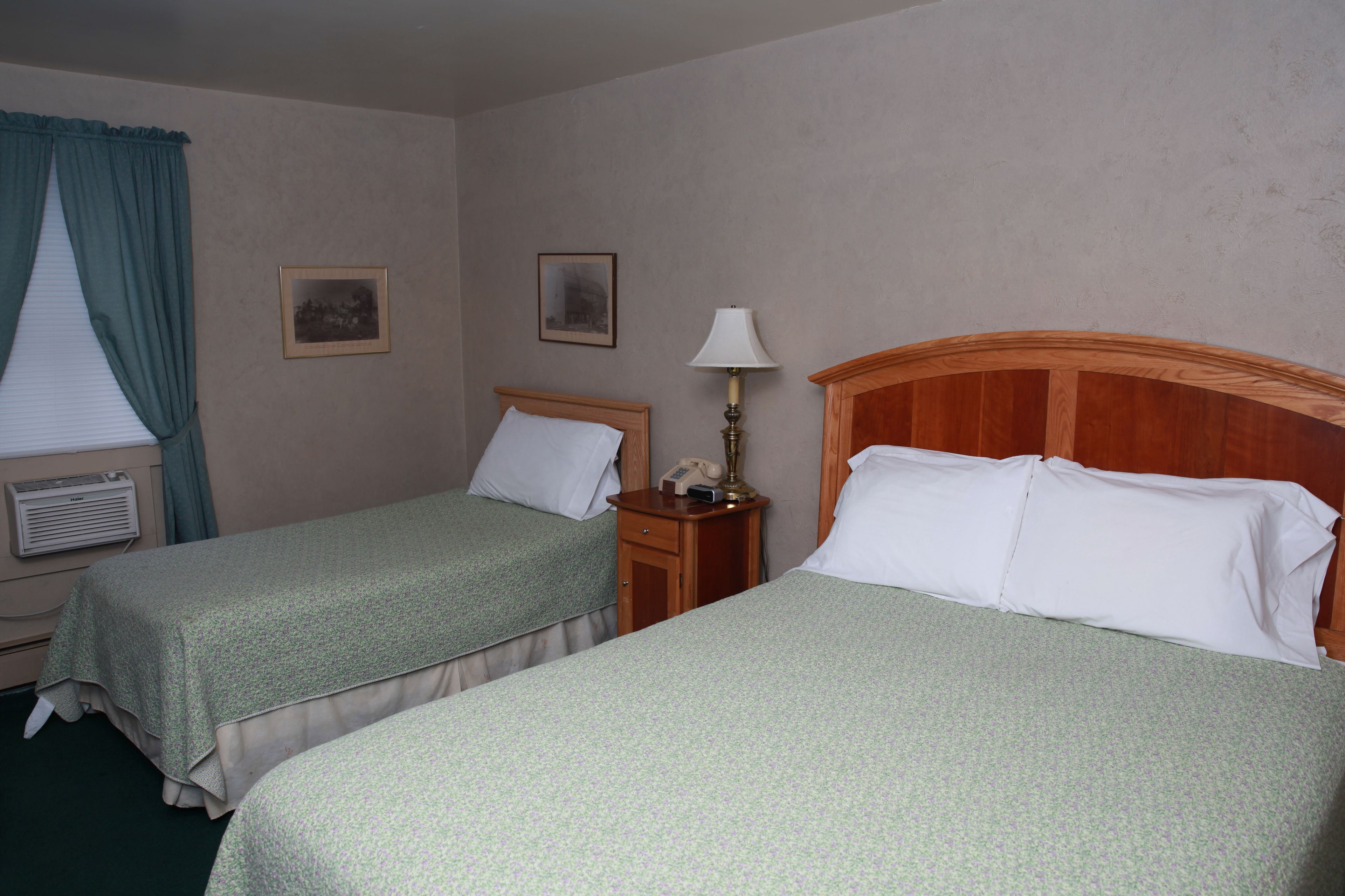 Una habitación de hotel con dos camas individuales, una mesita de noche con lámpara, un teléfono y dos cuadros en la pared.