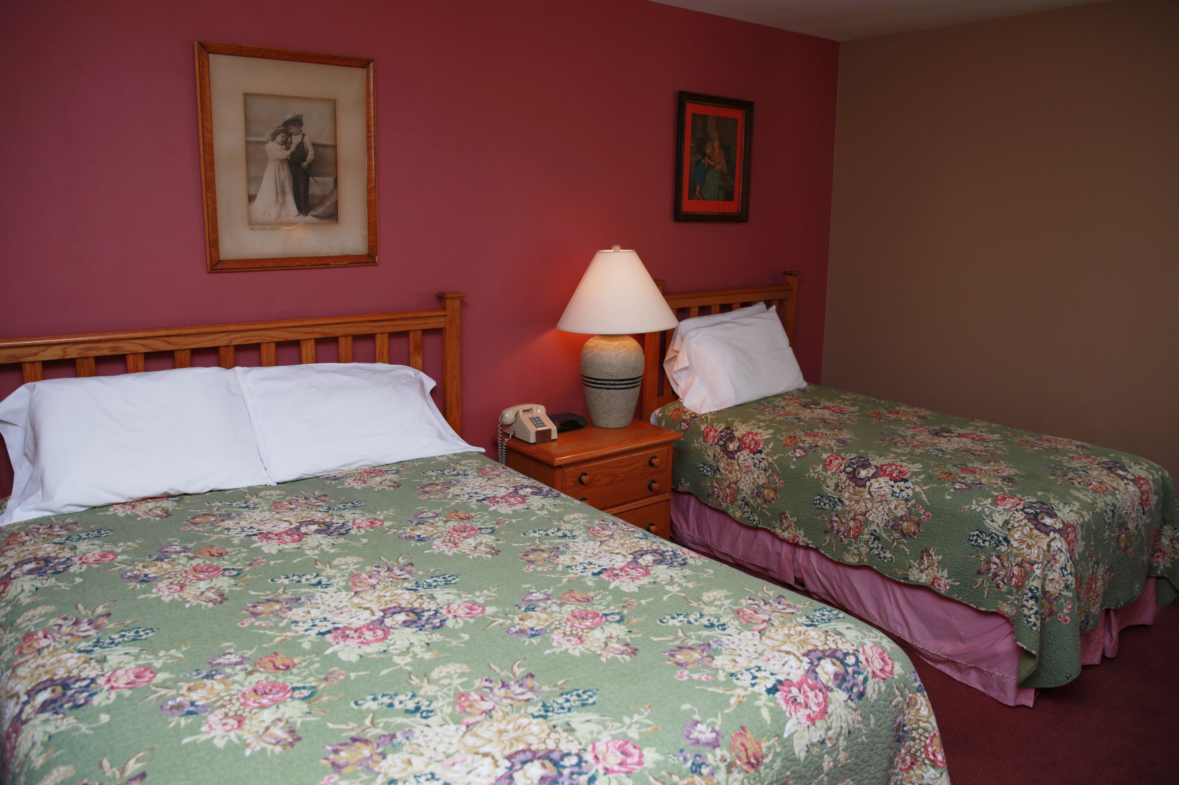 Una habitación con dos camas, cada una con ropa de cama estampada, una mesita de noche con lámpara y un cuadro enmarcado en la pared.