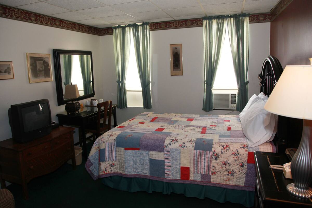 A hotel room with a bed, a television, a desk, and a lamp.