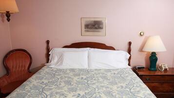 A bedroom with a bed, a wooden chair, a nightstand with a lamp, and a framed picture on the wall.