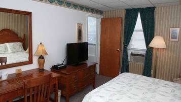 Habitación de hotel con cama, cómoda de madera, televisor, escritorio con lámpara y espejo.