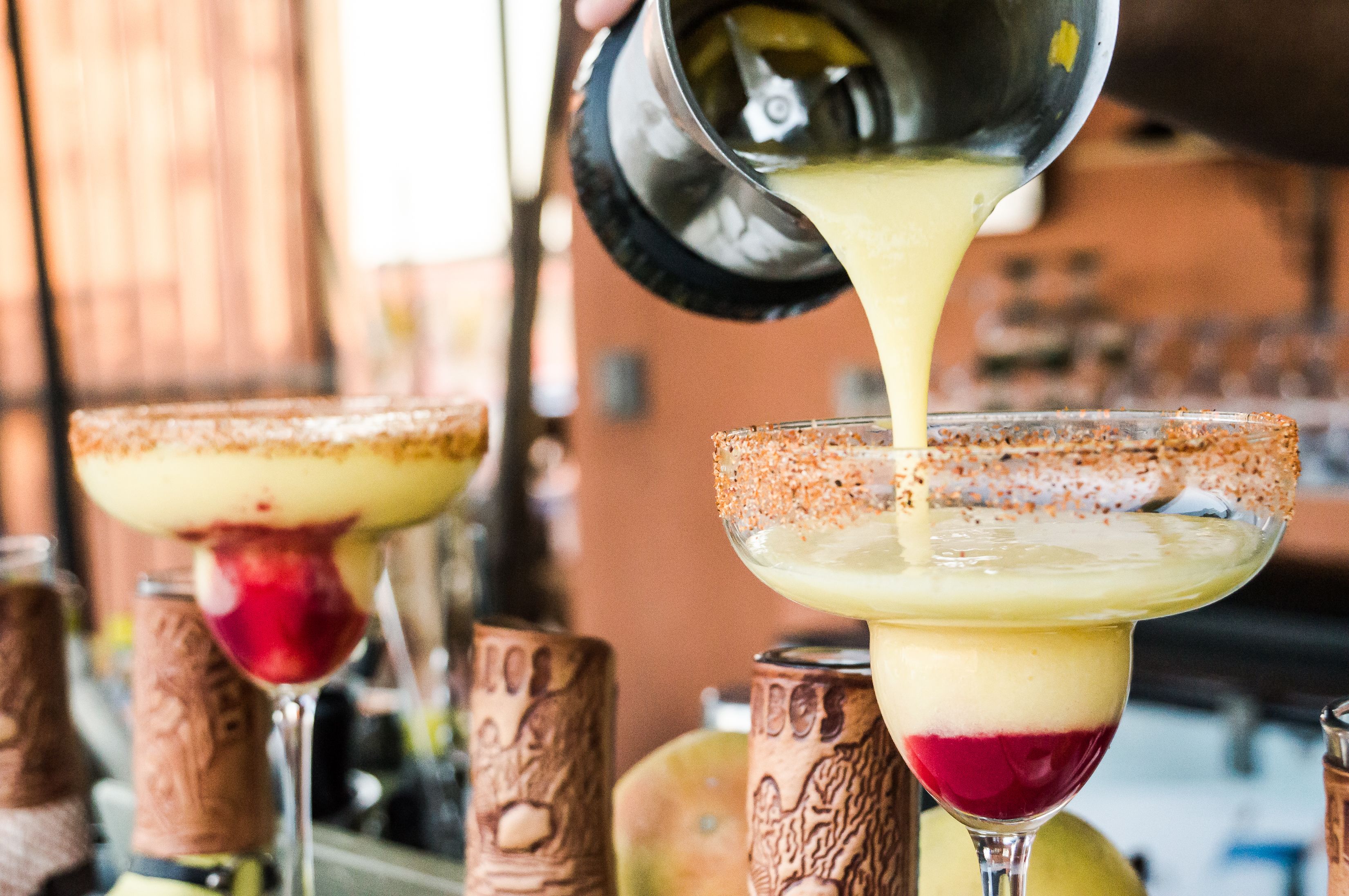 A bar setting with a drink being poured into a margarita glass.
