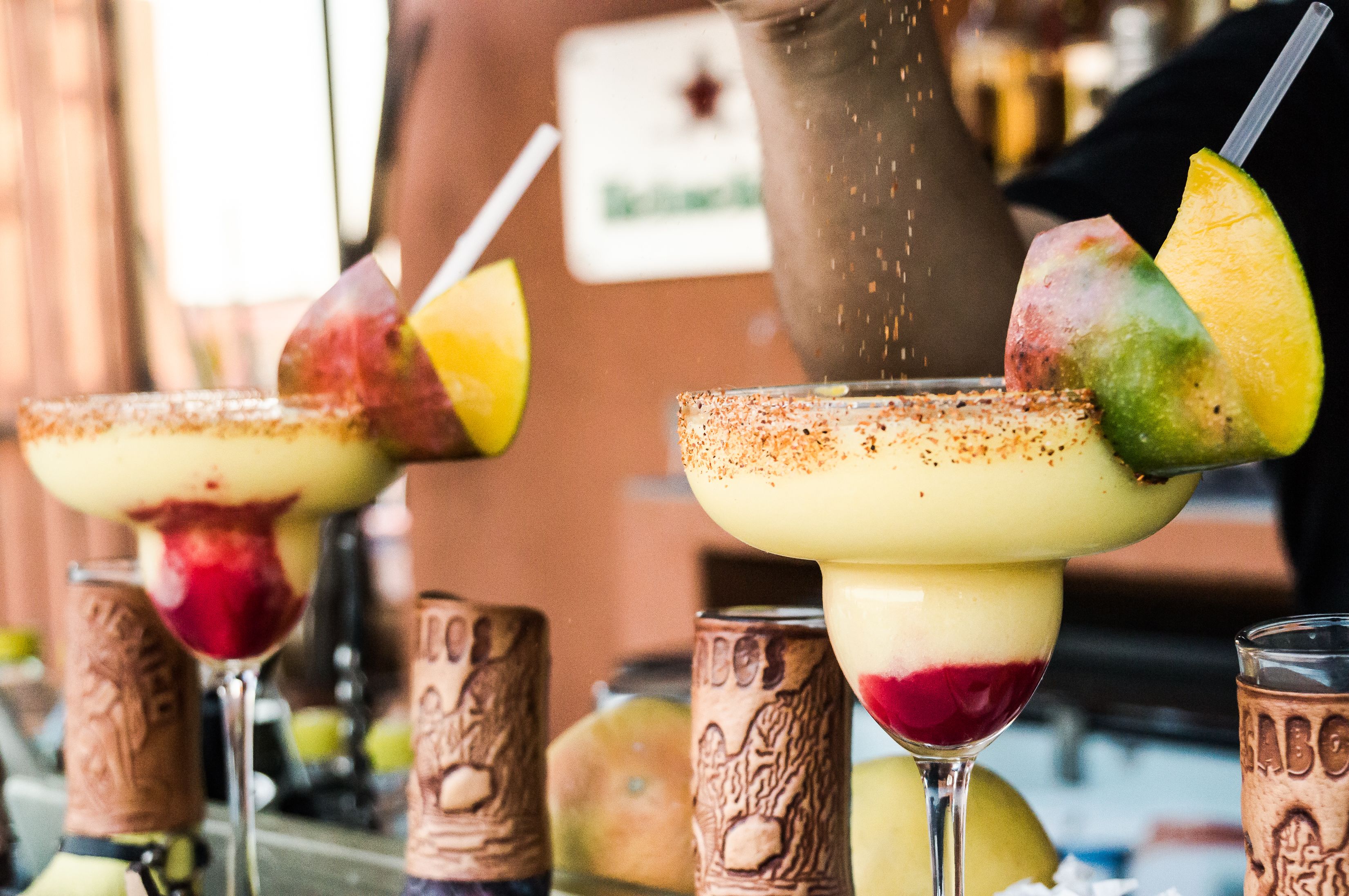 Três coquetéis com guarnições de frutas e uma área de bar com garrafas de marca.