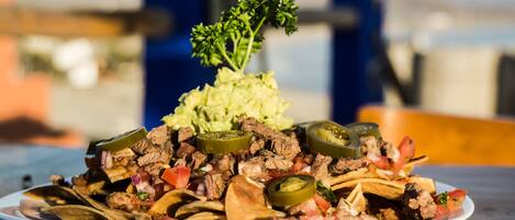Un plato de nachos con diferentes ingredientes, como carne, queso y jalapeños, servido en un plato blanco.