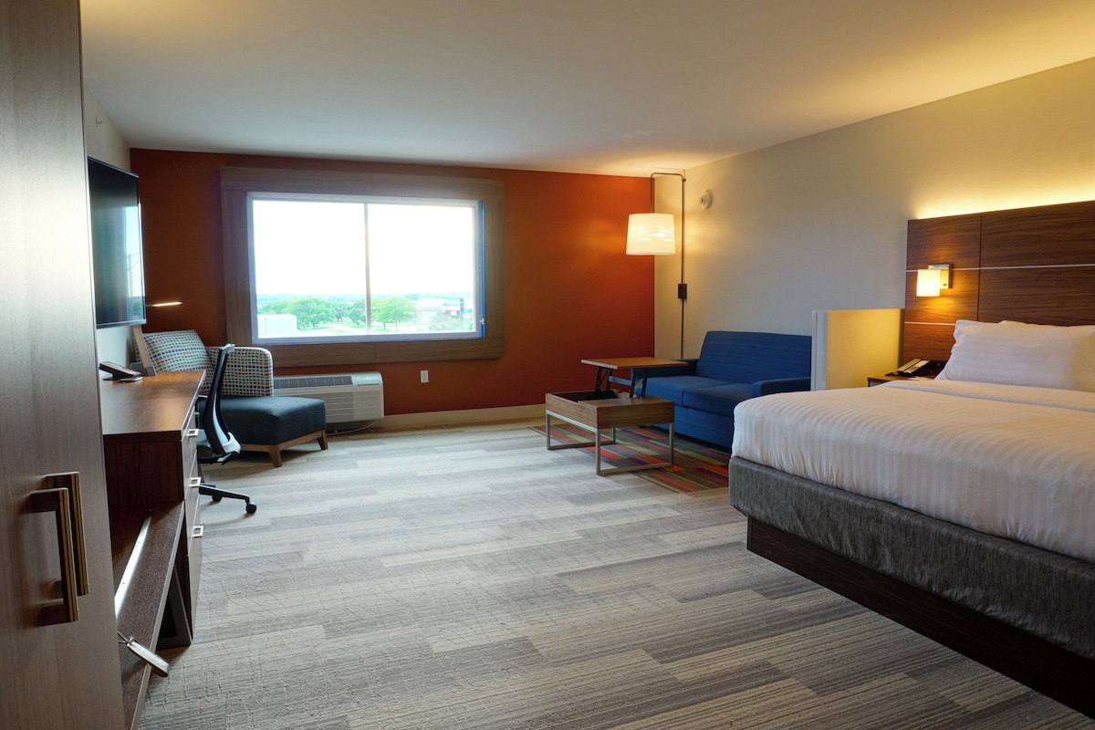 A hotel room with a bed, a desk, a chair, a sofa, and a large window.