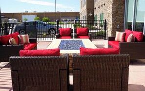 An outdoor seating area with wicker furniture and red cushions, a fire feature, and a view of a building in the background. - Holiday Inn Express & Suites Omaha - Millard Area by IHG (Omaha)