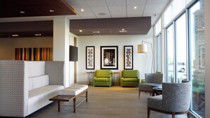 A modern hotel lobby with a sectional sofa, two armchairs, a small table, and artwork on the walls.