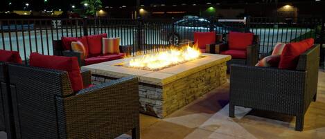 Un área de estar exterior con mobiliario de mimbre y una chimenea central.