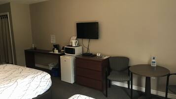 A hotel room with a bed, a desk with a microwave, a chair, a small table, and a television on the wall.