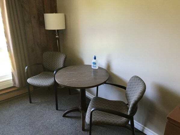 Habitación de hotel con dos sillones tapizados, una mesa redonda, una lámpara y un dispensador de gel antibacterial.