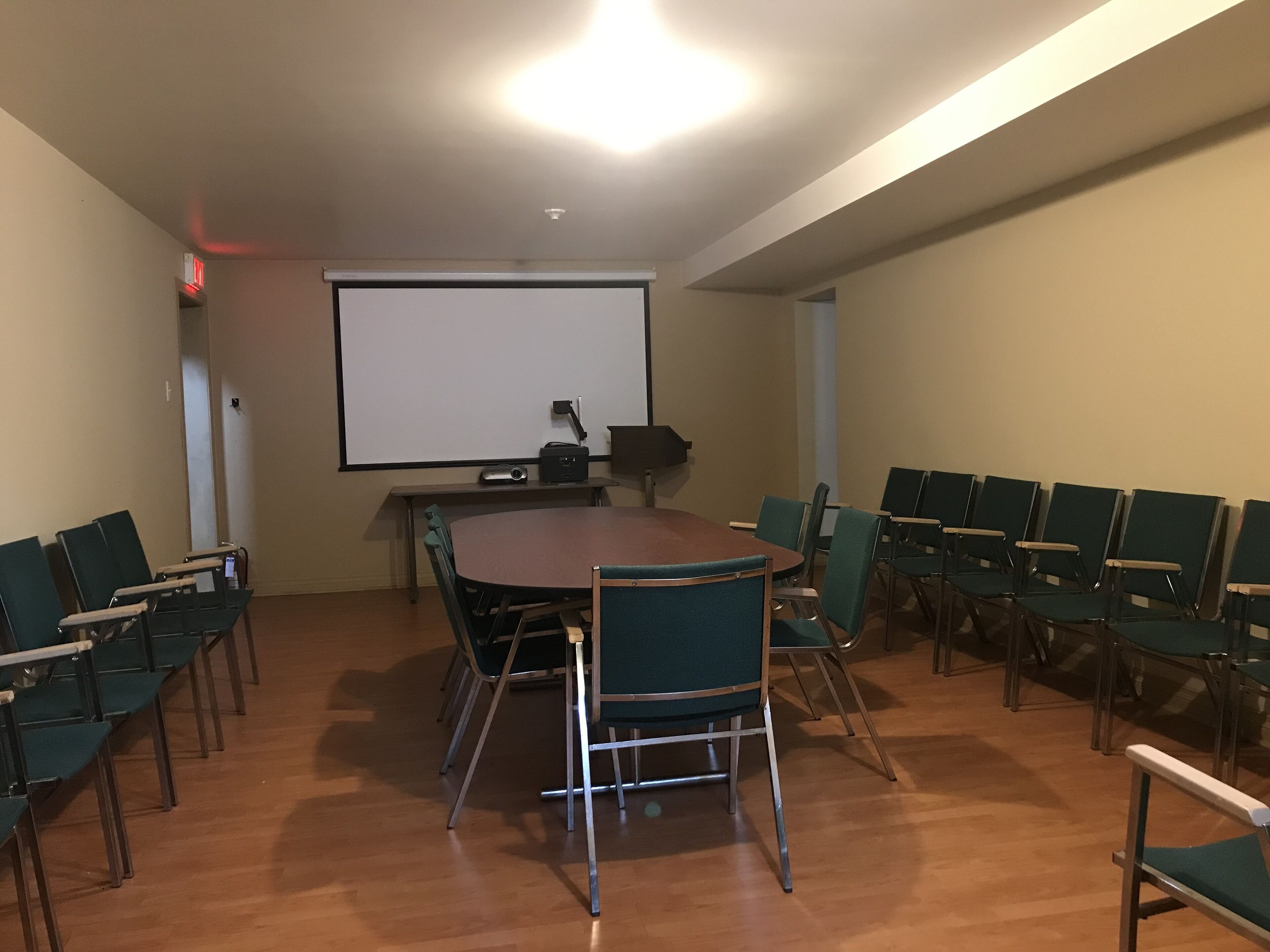 A conference room with a large table, chairs, a projector screen, and a whiteboard.