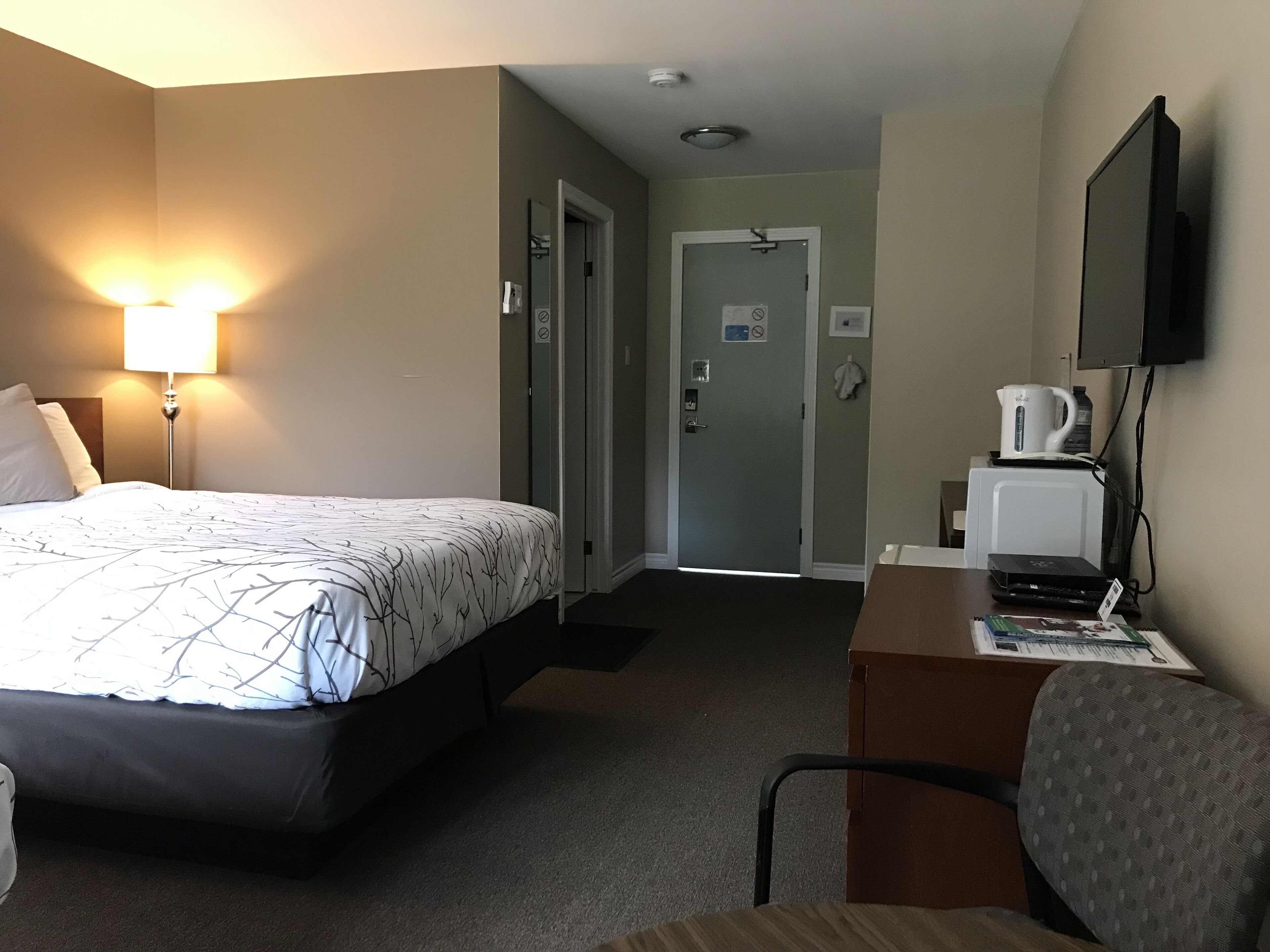 A hotel room with a bed, a desk, a chair, a lamp, a television, and a coffee maker.