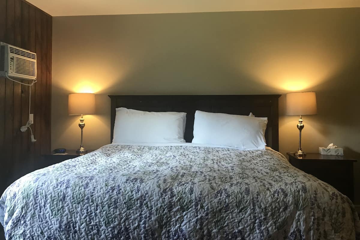 Un lit bien fait, recouvert d’une couvre-lit à motifs floraux, avec deux oreillers blancs et deux lampes de chevet de chaque côté.