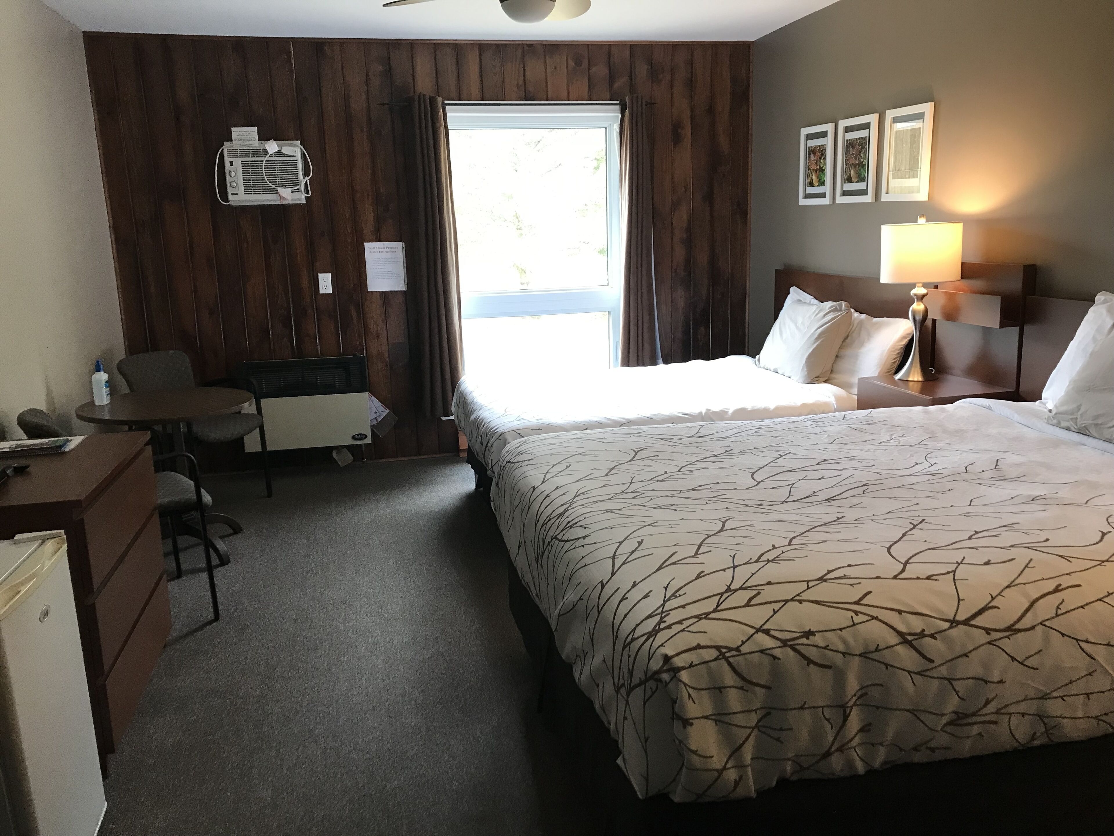 Una habitación de hotel con cama, escritorio, silla, lámpara y ventana.