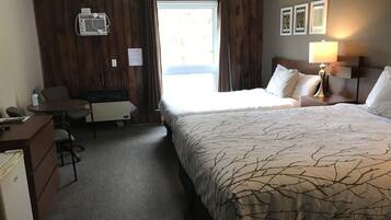 Una habitación de hotel con cama, escritorio, silla, lámpara y ventana.