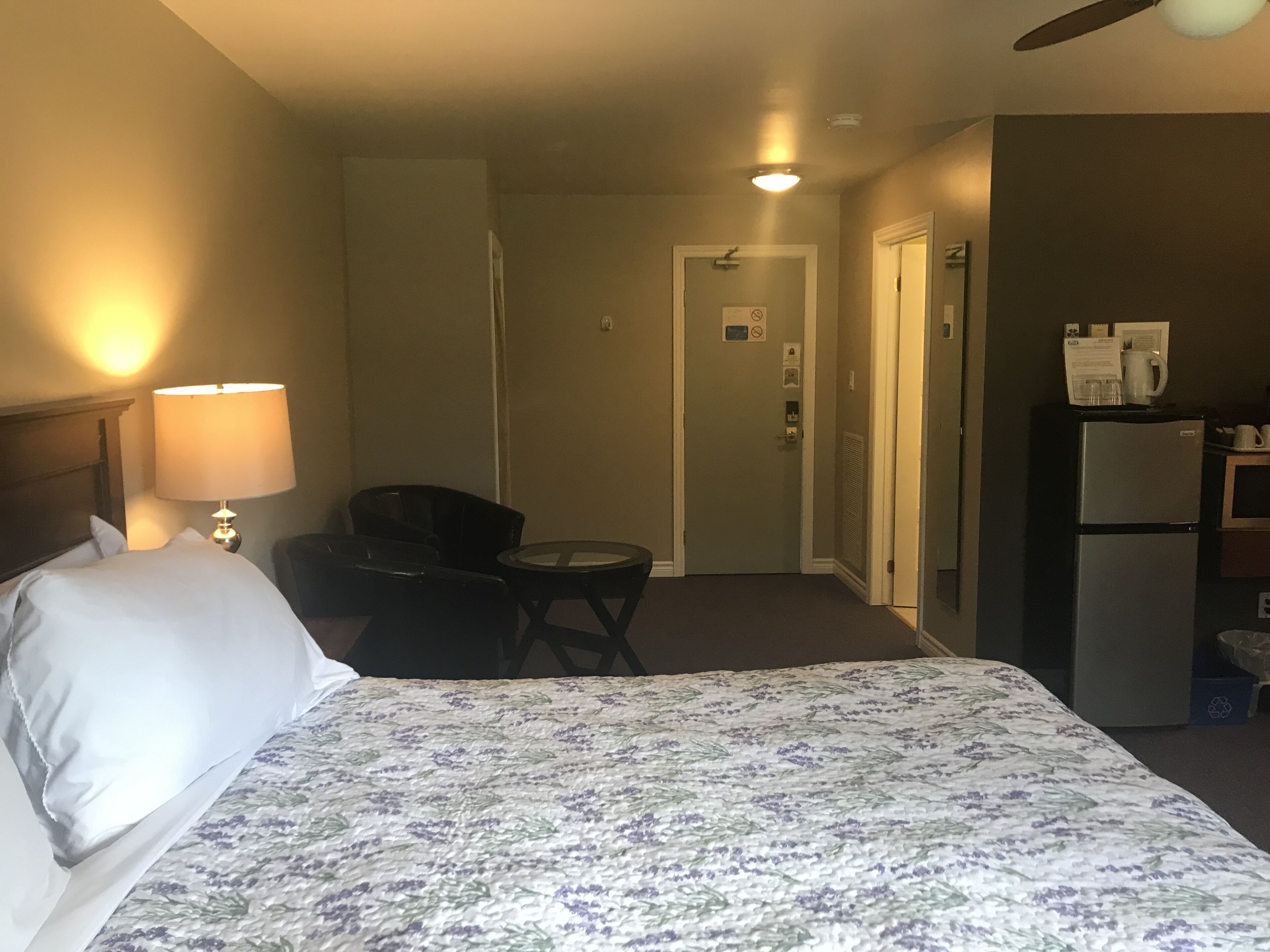 Una habitación de hotel con cama, escritorio, silla, refrigerador y microondas.