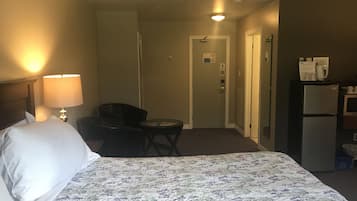 Una habitación de hotel con cama, escritorio, silla, refrigerador y microondas.