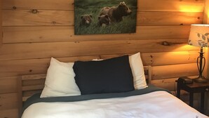 Habitación de cabaña de madera con cama, almohadas, una lámpara y un cuadro de un oso en la pared.