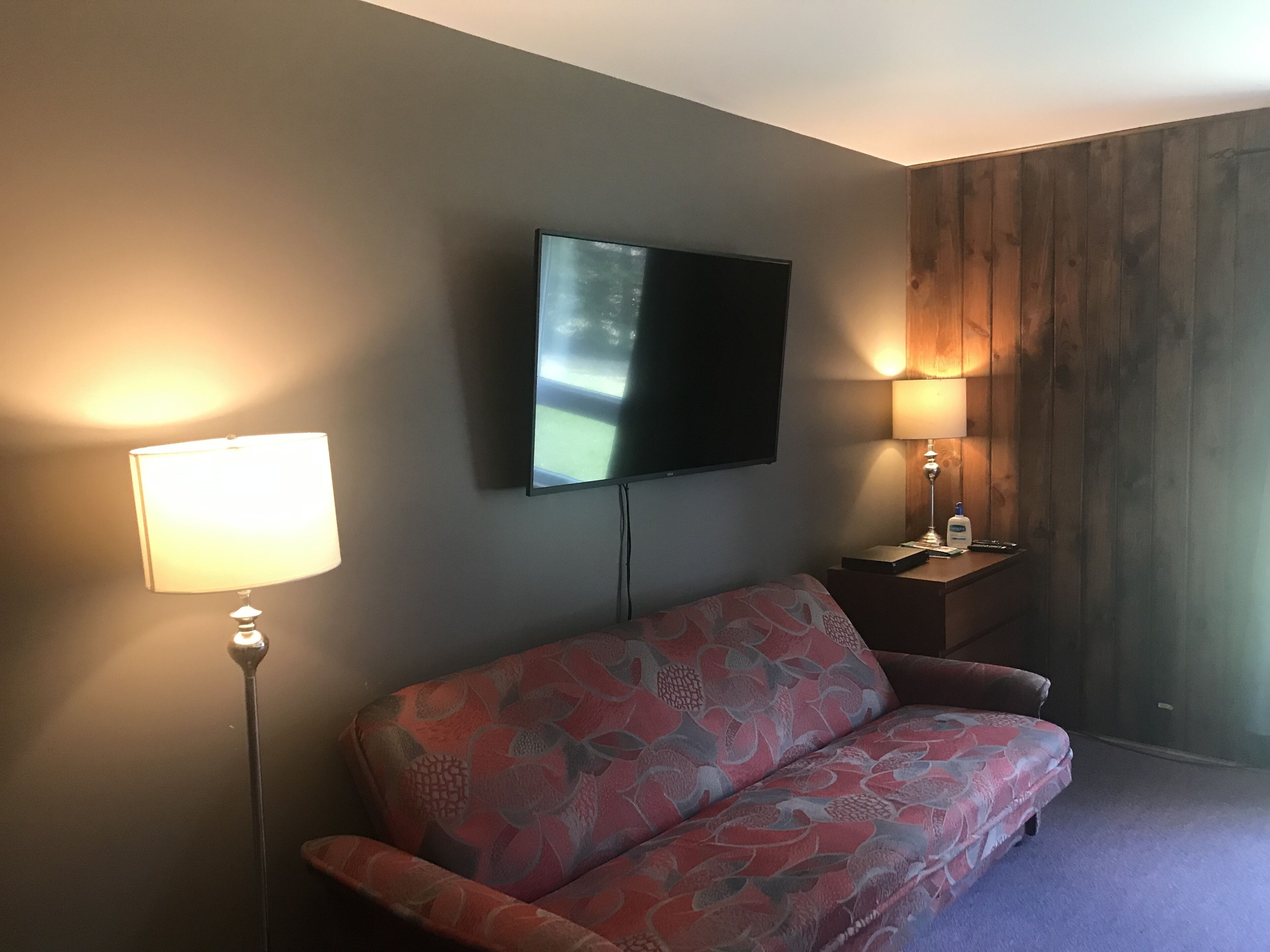 Ett modernt vardagsrum med en soffa, en platt-TV som är monterad på väggen och två sänglampor på ett nattduksbord i trä.