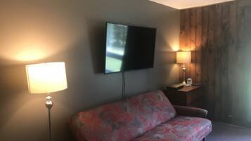 Ett modernt vardagsrum med en soffa, en platt-TV som är monterad på väggen och två sänglampor på ett nattduksbord i trä.