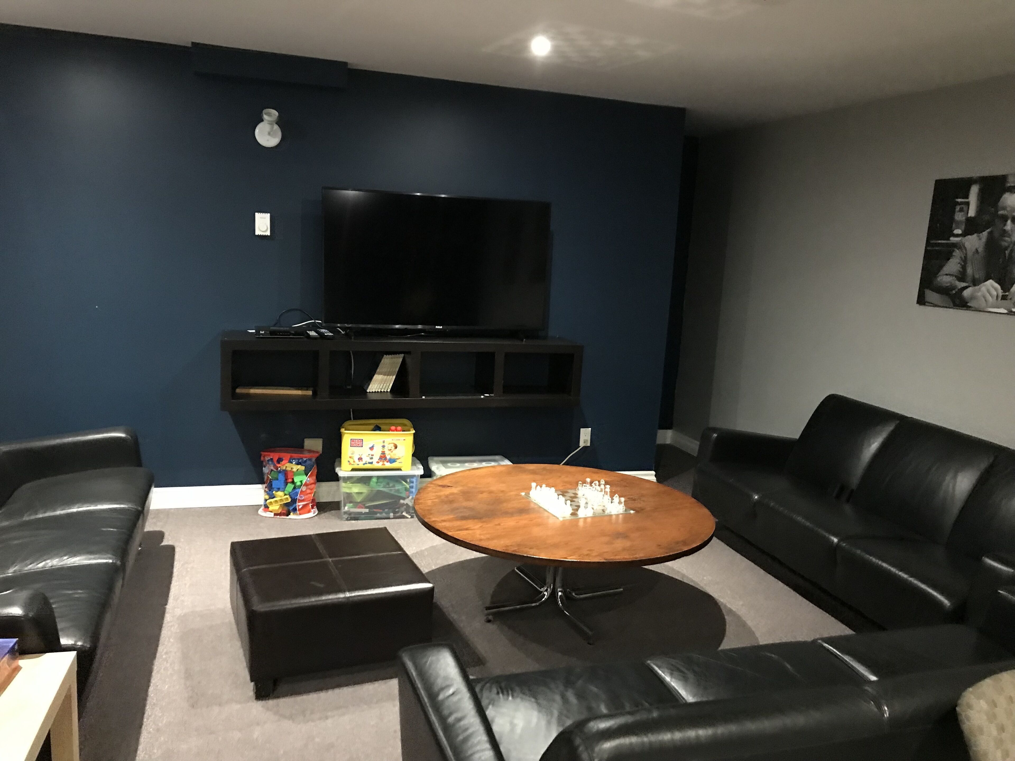 A living room with a TV, black leather sofas, a coffee table, and a bookshelf.