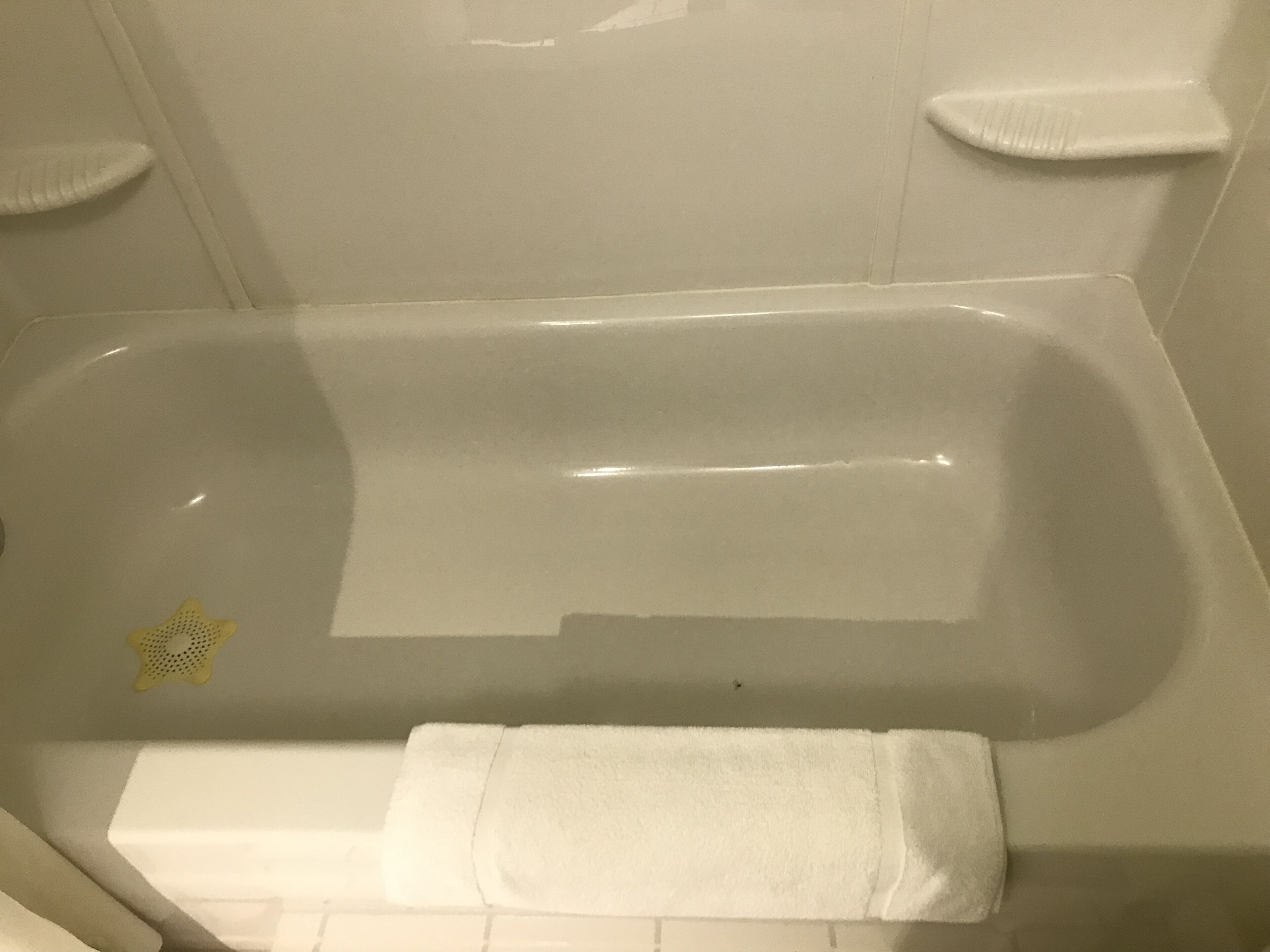 Une salle de bain avec une baignoire, une serviette blanche et un objet jaune en forme d’étoile sur le sol.