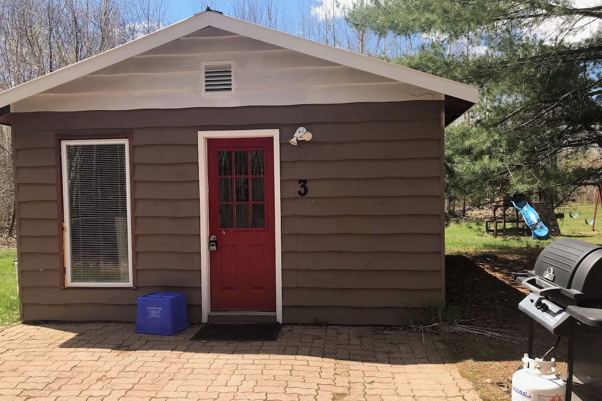 Une petite cabane à un seul étage, avec une porte rouge, une fenêtre avec des stores et le chiffre « 3 » peint sur la porte.