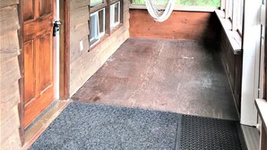Una cabaña de madera con una hamaca, una puerta de madera y ventanas grandes.