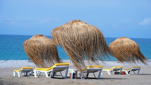 Ein Strand mit Strohdächern und gelb-weißen Liegestühlen.