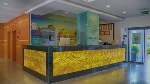 A reception desk with a modern design, a control panel, and a wall with a colorful mural. - Club Aqua Plaza (Alanya)