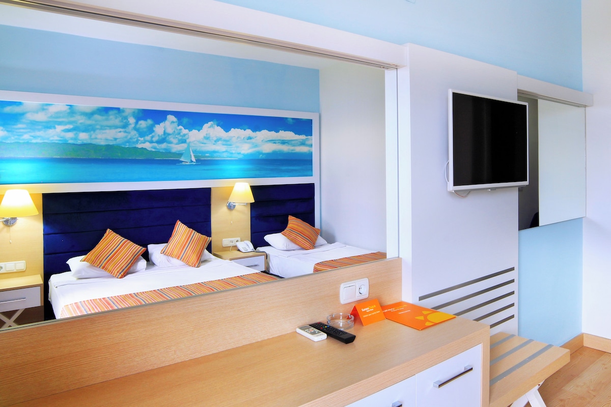 A hotel room with a bed, a TV, and a desk with a remote control.