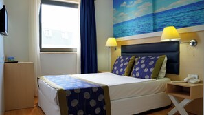 Une chambre d’hôtel comprenant un lit, deux lampes de chevet, un téléphone, une table de chevet, une fenêtre avec des rideaux et une fresque murale représentant l’océan.