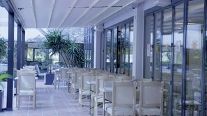 Un espace extérieur aménagé, abrité et doté de chaises et de tables, de grandes fenêtres et de plantes en pot.