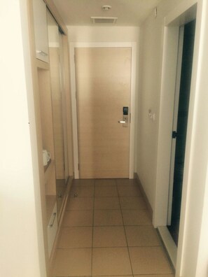 En smal hall med en dörr längst in, en ljusströmbrytare på väggen och en ventilationsöppning i taket.