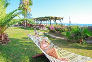 A hammock in a grassy area with a view of the sea and a covered seating area in the background. - Club Aqua Plaza (Alanya)