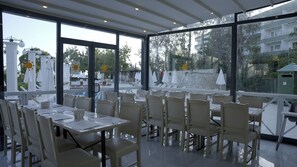 A restaurant with outdoor seating, large windows, and a view of the surrounding area. - Club Aqua Plaza (Alanya)