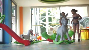Un niño jugando con caballos de juguete y un tobogán en un espacio interior bien iluminado.