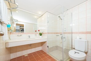 A modern bathroom with a glass shower enclosure, a white sink with a mirror above, and a toilet with a paper towel holder. - Club Aqua Plaza (Alanya)