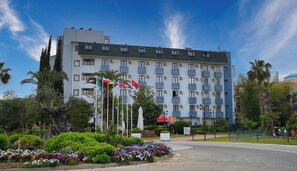 Un hotel a più piani con balconi, immerso in giardini curati e palme.