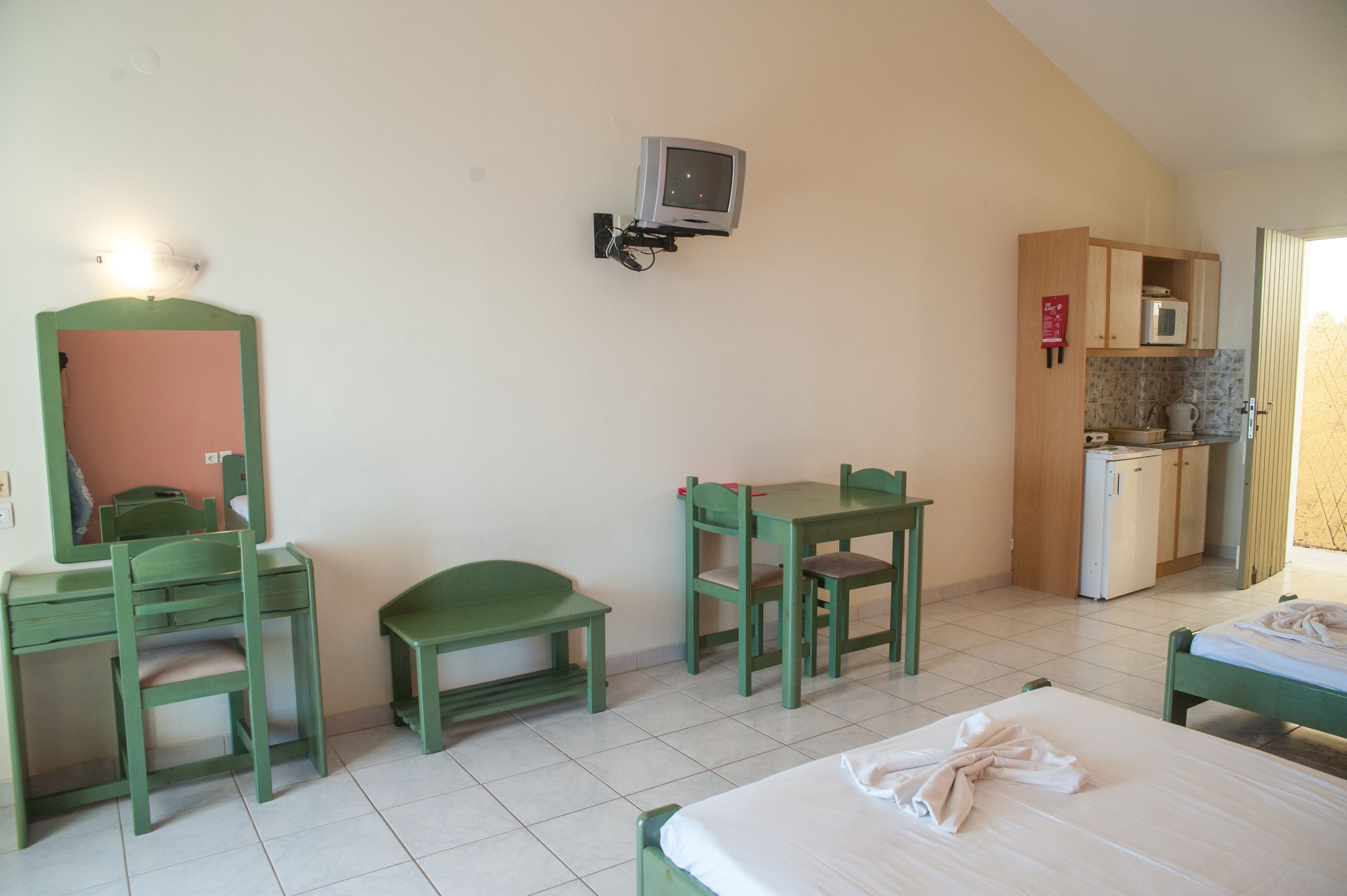 A room with a bed, a desk, a chair, a small table, a microwave, and a television mounted on the wall.