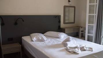 A hotel room with a bed, a bedside table, a nightstand, a desk, a mirror, and a window with curtains.