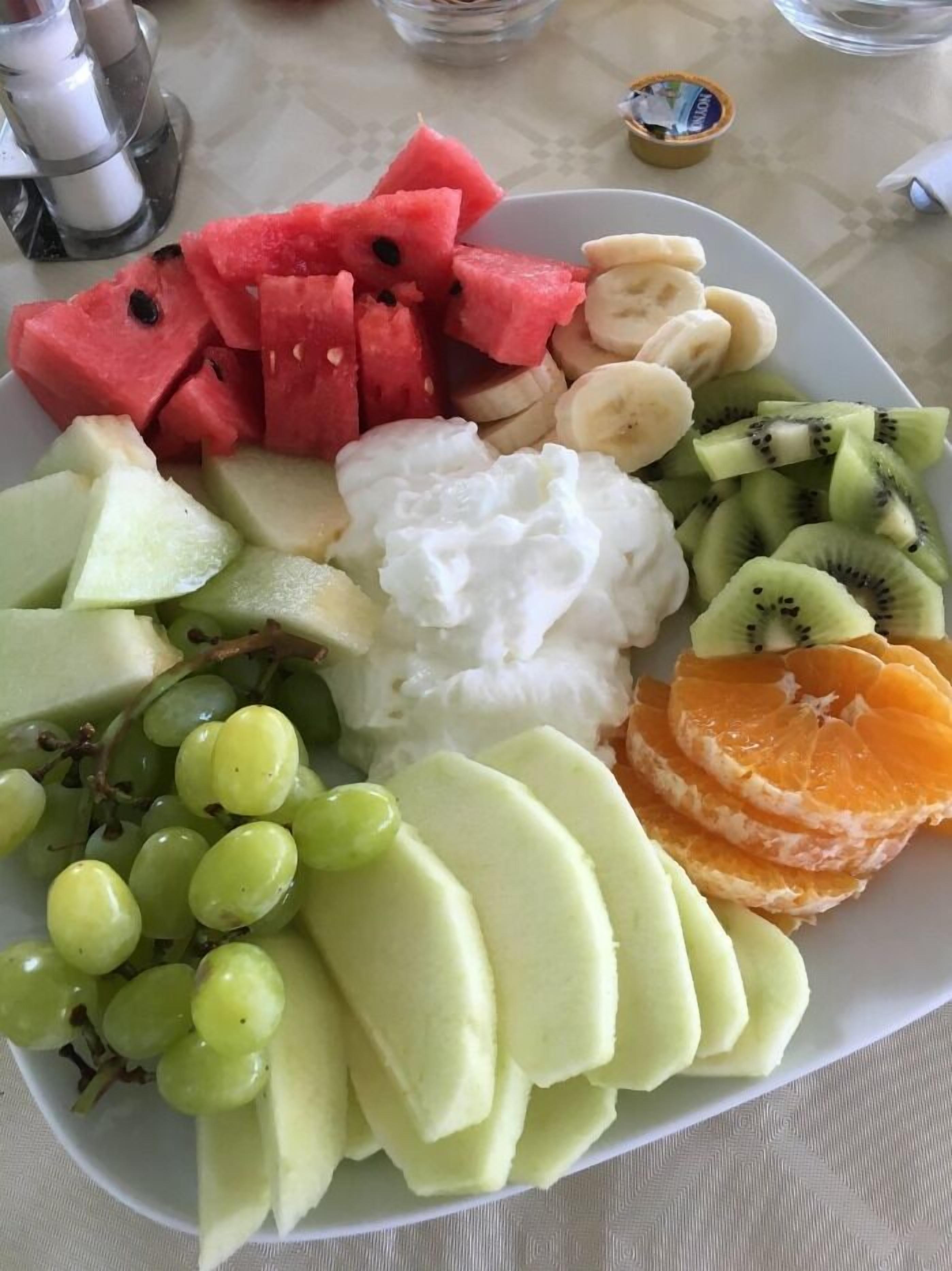 A plate of assorted fruits including watermelon, bananas, kiwi, grapes, melon, and orange slices.