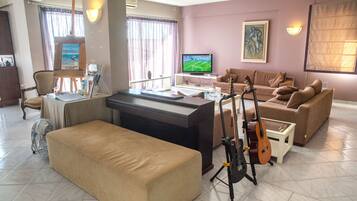 A living room with a TV, a guitar, a couch, and a fan.