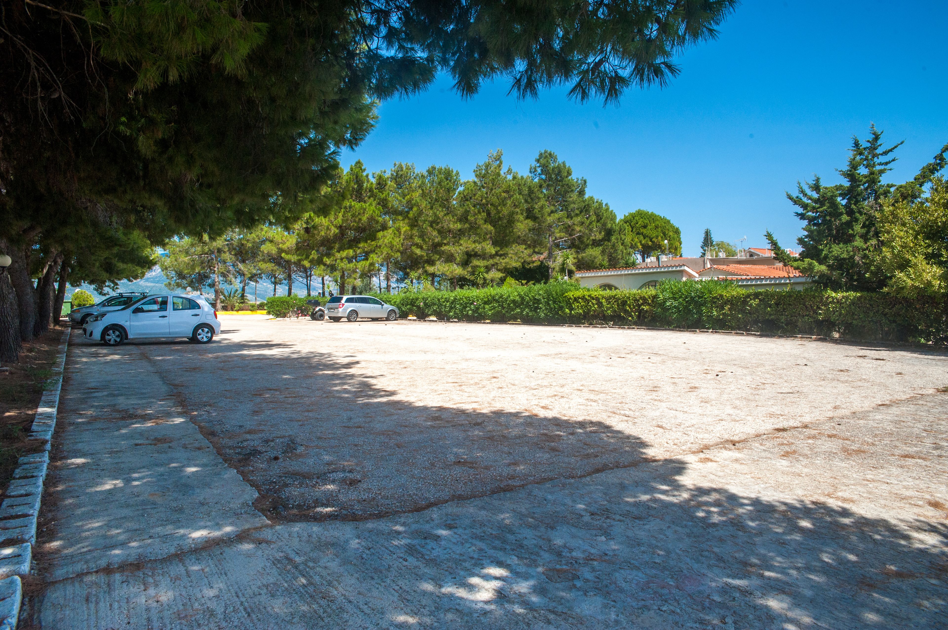 A parking area with two cars, surrounded by trees and a building with a red roof.