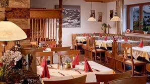 A restaurant with wooden tables and chairs, a stone wall, and a mountain painting on the wall. - Lifthotel (Kirchberg in Tirol)