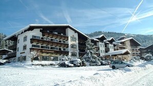 A multi-story hotel with a restaurant on the ground floor, surrounded by snow-covered trees and parked cars. - Lifthotel (Kirchberg in Tirol)