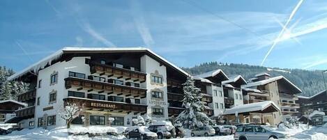 A multi-story hotel with a restaurant on the ground floor, surrounded by snow-covered trees and parked cars.