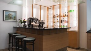 Una zona de bar con taburetes, una máquina de café y estantes con botellas y vasos.